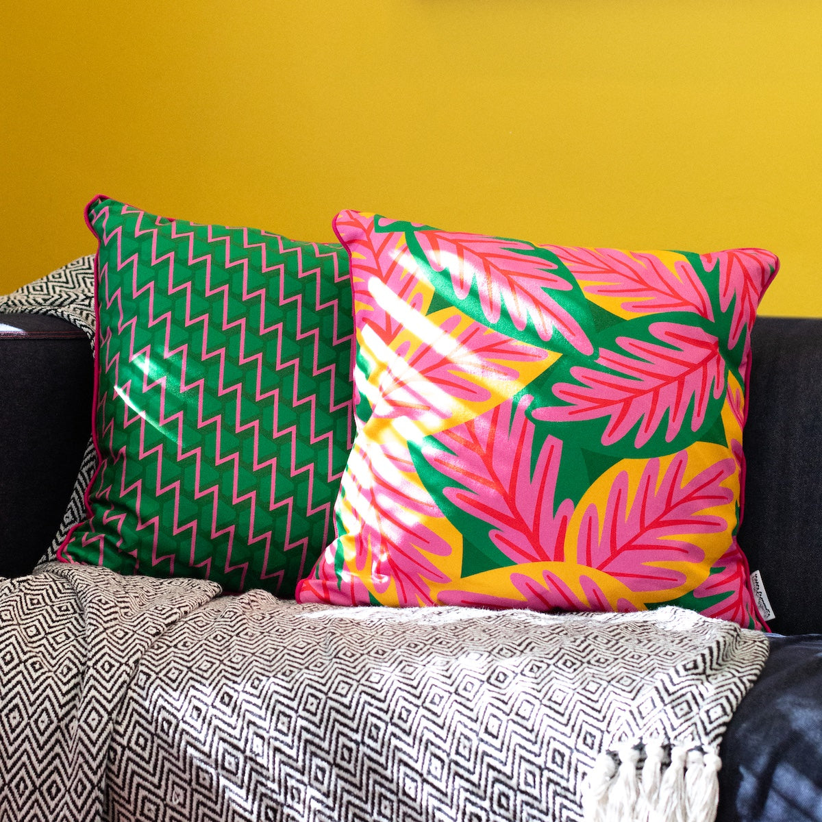 Colourful cushion cover duo on sofa with bold pink, yellow and green tropical leaves and geometric zigzag prints – Republic of Happy