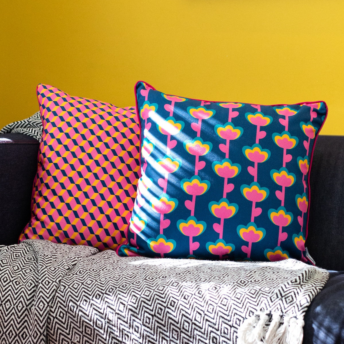 Colourful cushion cover duo on sofa with bold pink, yellow and green tropical leaves and geometric zigzag prints – Republic of Happy
